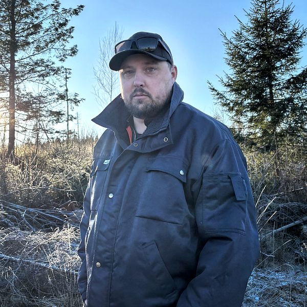 Person i mörk jacka och keps står i ett frostigt skogsområde med solen i bakgrunden.