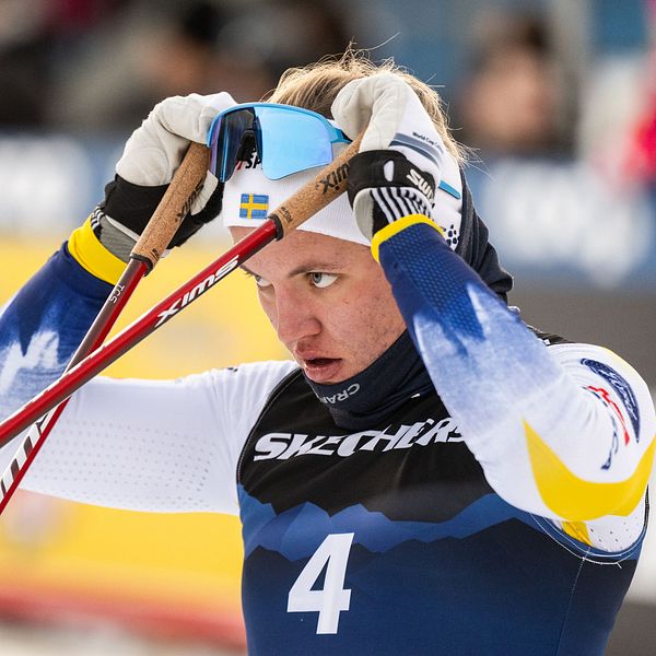 Skidåkare i tävlingsdräkt med nummer 4 dricker ur blå flaska.
