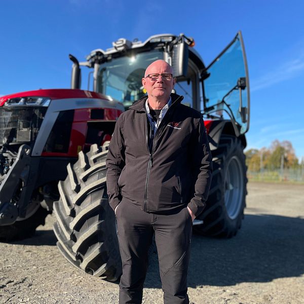 Självkörande traktor i ett öppet landskap. Traktorn har stora däck och är i gott skick, med förarhytten öppen. Himlen är klar och blå, vilket ger en ljus och solig atmosfär i bakgrunden.