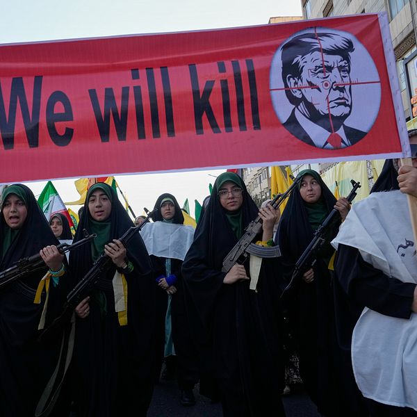 Iranska kvinnor med automatvapen demonstrerar under en banderoll med dödshot mot Donald Trump
