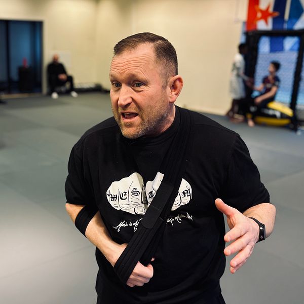 Personer tränar kampsport i en dojo med grå mattor och flaggor på väggarna. I förgrunden Jörgen Hamberg, ordförande för Västerås fight club.