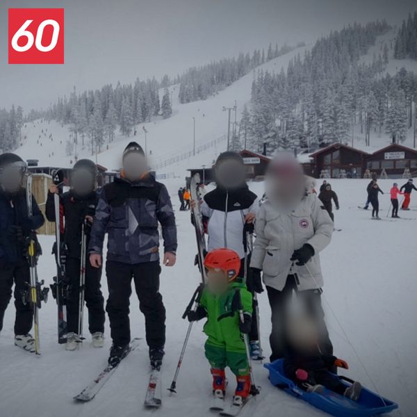 En grupp personer i skidkläder står samlade i en skidbacke vid snötäckta fjäll.