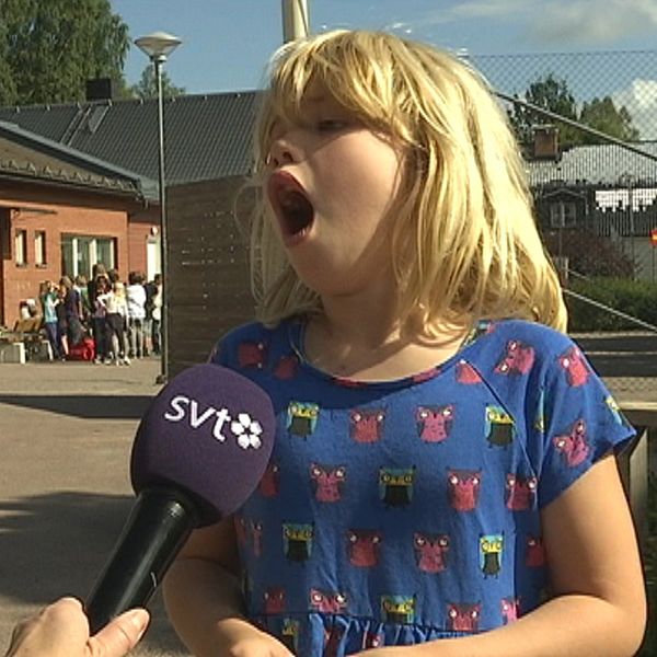 ung flicka intervjuas på skolgård, grimaserar med öppen mun