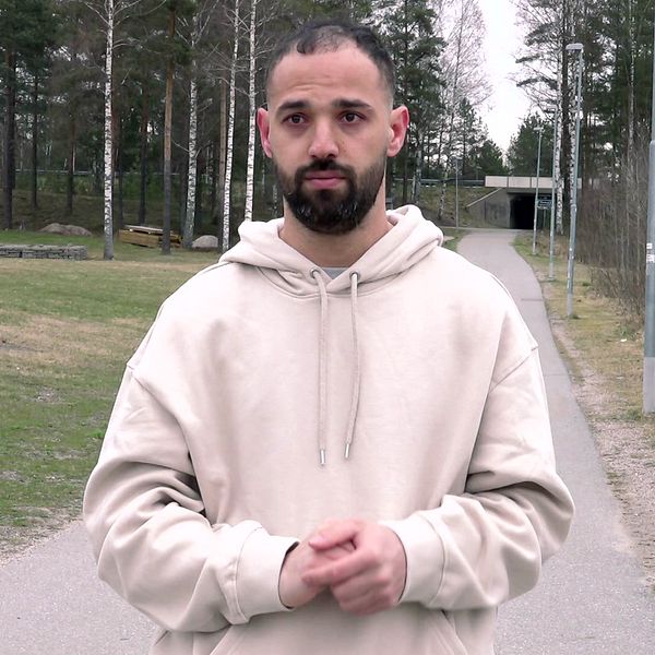 Maruf Mohammadi i beige hoodie står på gångväg i utomhusmiljö med träd i bakgrunden.