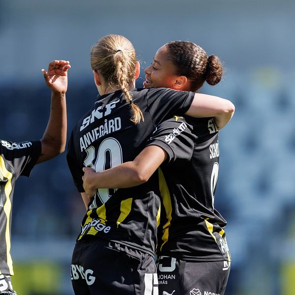 Tre fotbollsspelare i svartgula matchställ firar tillsammans på planen.