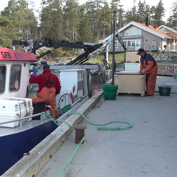 Två fiskare står vid en fiskebåt i Bondhamn