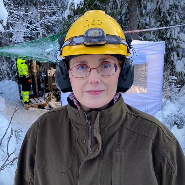 Helena Karlsson, geolog på Aura Energy står med en gul bygghjälm framför ett provborrningshål.