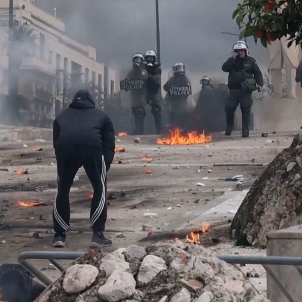 Våldsam protestscen med kravallpolis och brinnande barrikader i stadsmiljö.