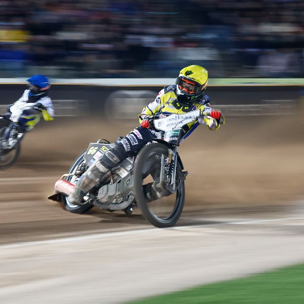 Två speedwaymotorcyklar med förare. Sanden yr.