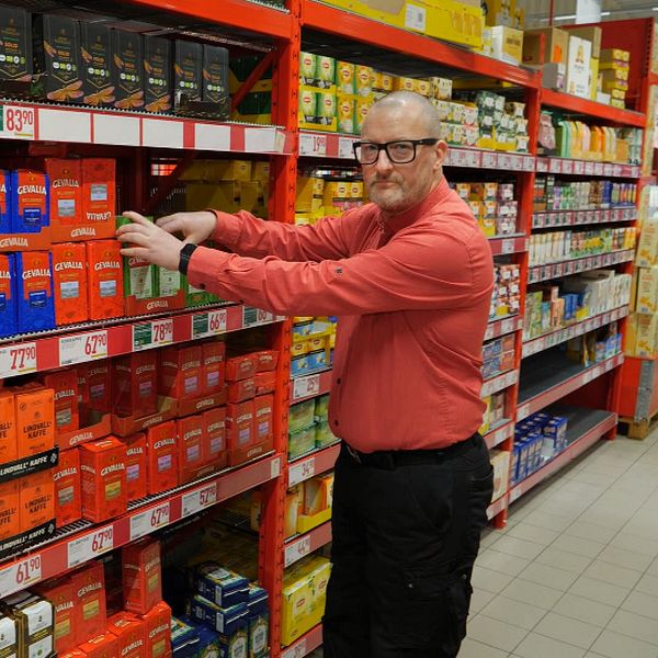 en man i röd skjorta sorterar kaffepaket på en hylla i en butik