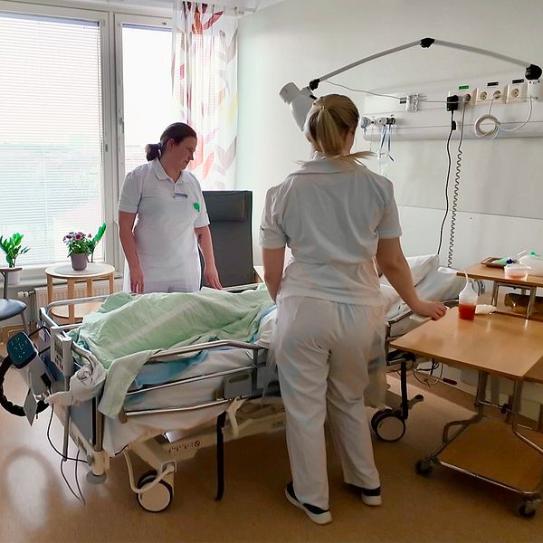 Två sjuksköterskor vårdar en patient i ett sjukhusrum med utrustning.