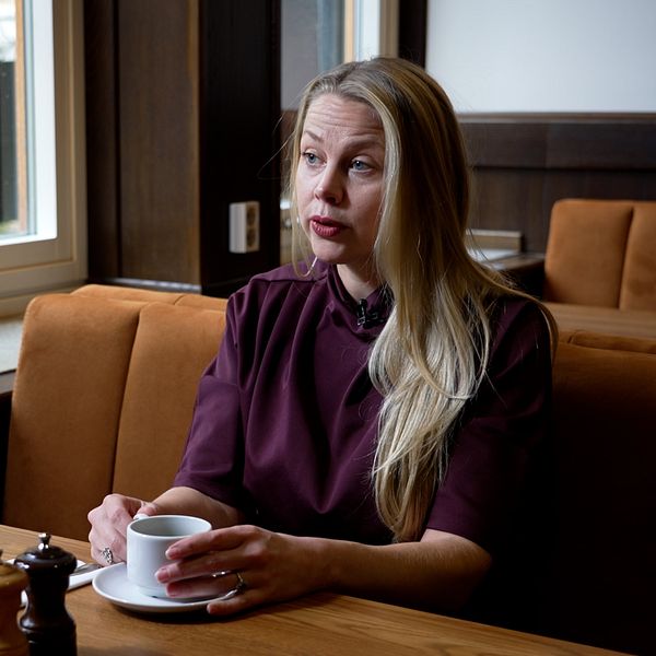 Annie Ross sitter vid ett bord och talar i en restaurang