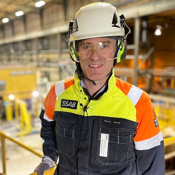 SSAB-anställd man i hjälm framför stor industrihall i Borlänge.