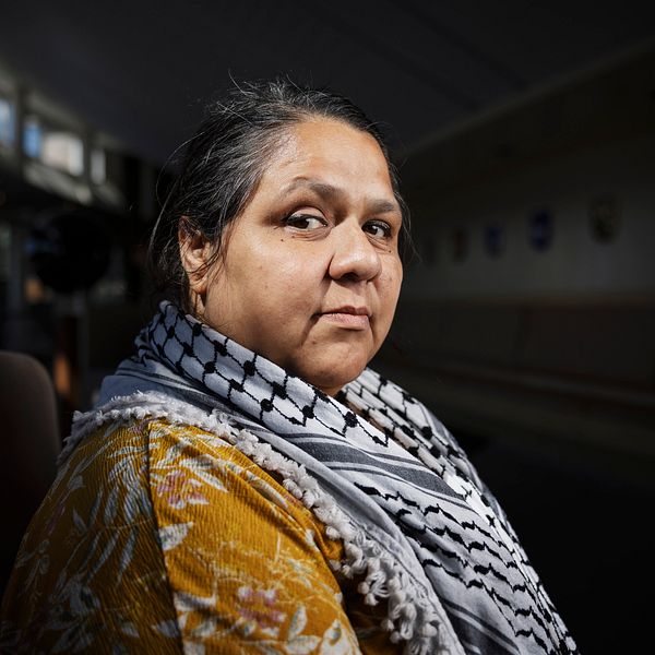 Person med palestinasjal sitter i ett svagt upplyst rum.