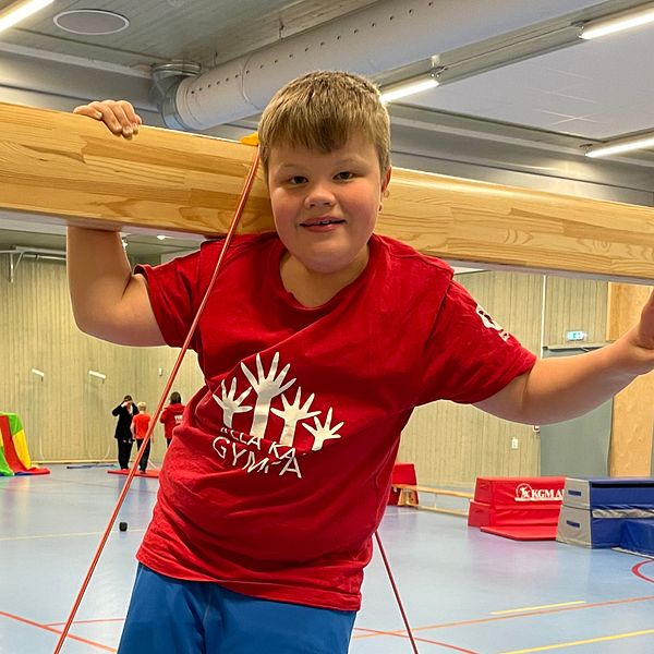 Barn i röd tröja i gymnastiksal med redskap och hinderbanor.