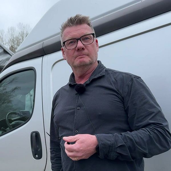 En person står framför en silverfärgad skåpbil utomhus.