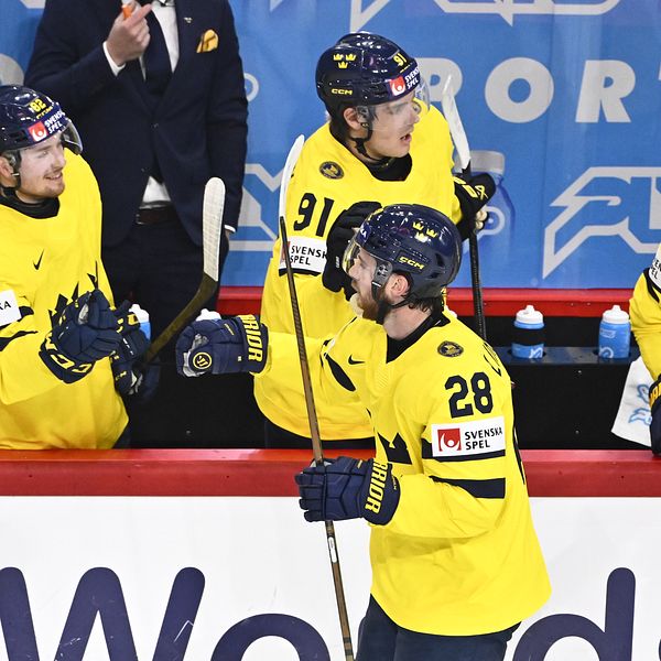 Ishockeyspelare i Tre Kronors gula tröjor firar vid båset under match.