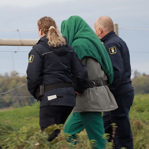 den misstänkta går med vakter runt området där den misstänkta brottsplatsen är.