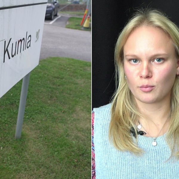 Skylt med texten ”Anstalten Kumla” är tydligt synlig i den vänstra delen av bilden, med en grön gräsyta i förgrunden och en del av en väg och parkering i bakgrunden. I den högra delen av bilden syns en person med långt, ljust hår, klädd i en tröja.