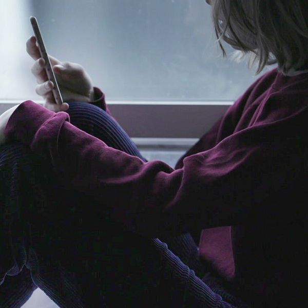 Flicka sitter i fönster och tittar på sin telefon