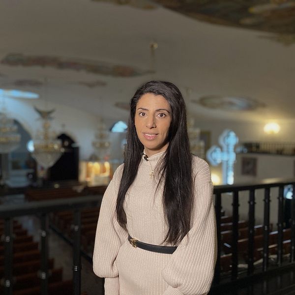 en kvinna i vit klänning och långt mörkt hår står i en kyrka