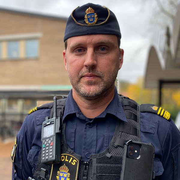Polis i uniform står framför en tegelbyggnad.