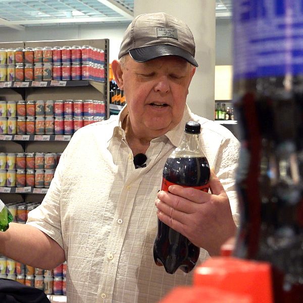 Person i butik väljer mellan två flaskor, en grön glasflaska och en svart plastflaska.