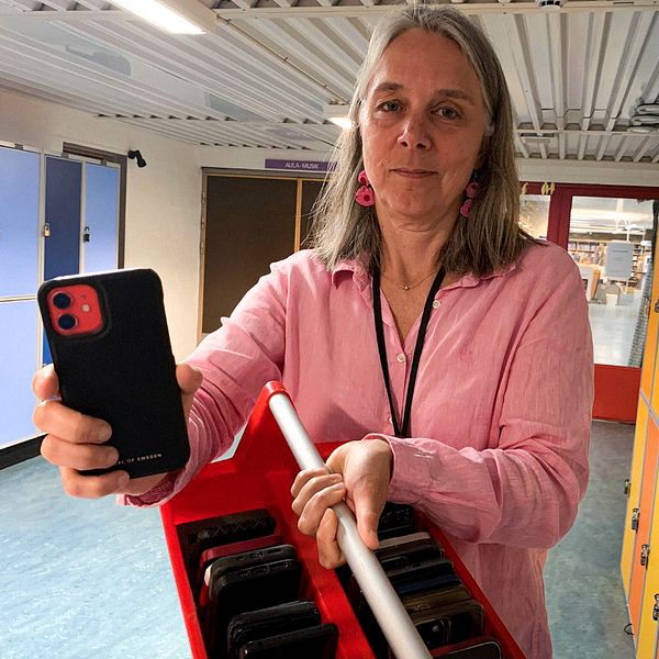 Bild på en rektor i en skolkorridor, hon håller upp en mobil.