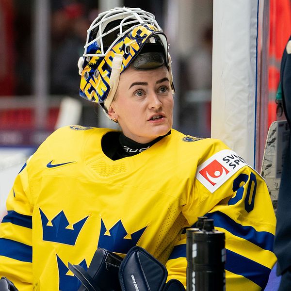 Hockeyspelare i gula tröjor vid rinken. Coach talar med en målvakt.