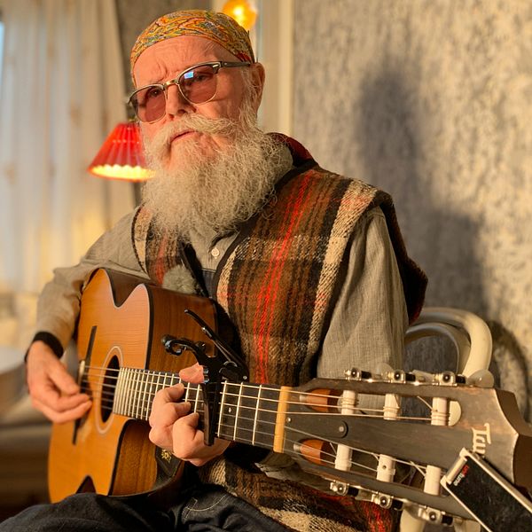 En skäggig man spelar gitarr vid ett bord.