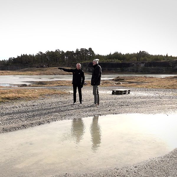 Två män står och pekar i ett gammalt stenbrott i Hejdeby