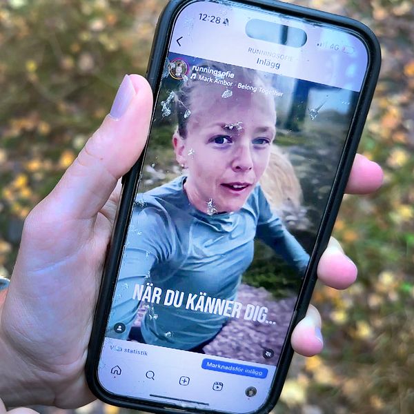 En hand som håller en mobiltelefon som visar ett Instagram-inlägg med en text som säger ”NÄR DU KÄNNER DIG...”. Bakgrunden består av höstlöv och naturlandskap.