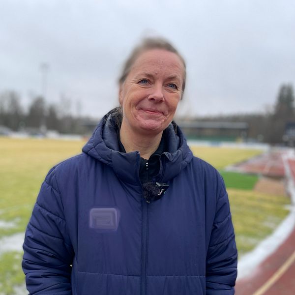 Kvinna i blå jacka står vid en fotbollsplan