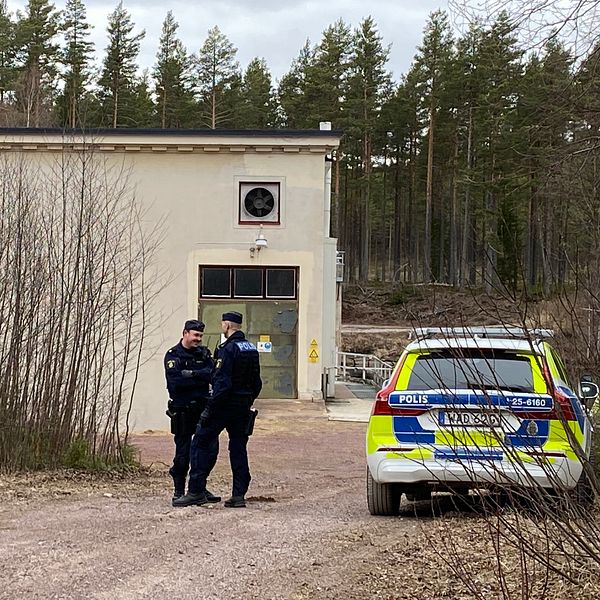 Två polisen står bredvid en polisbil vid en kraftstation