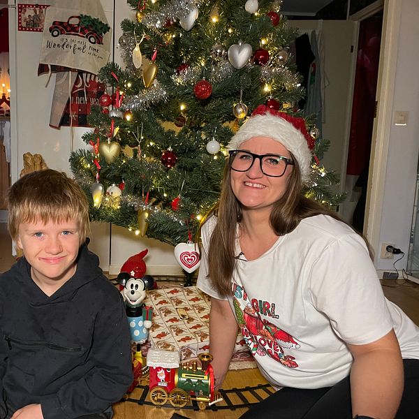 En kvinna och hennes son sitter framför en julgran i ett julpyntat hem.