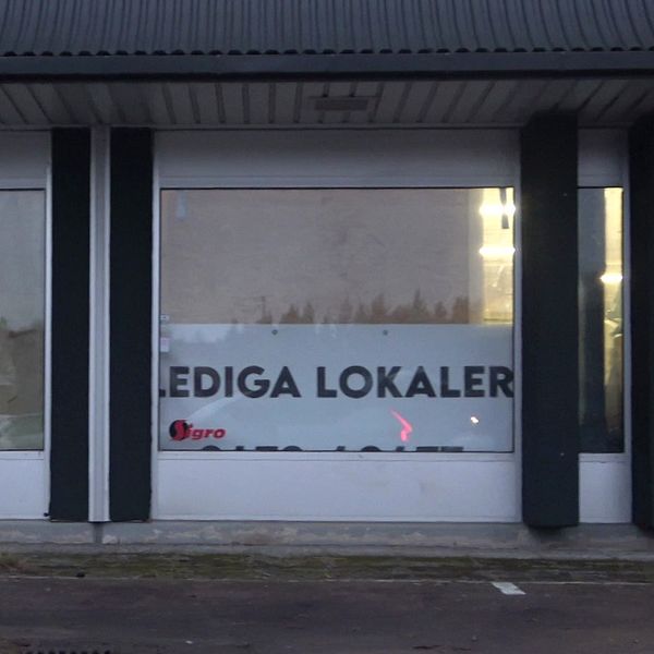 Skyltfönster med texten ”Lediga lokaler” i vit och svart färg, delvis täckt av smutsiga eller träningsskyddade fönster. Bakom fönstret syns suddiga konturer av vad som troligen är inredning eller föremål i lokalen.