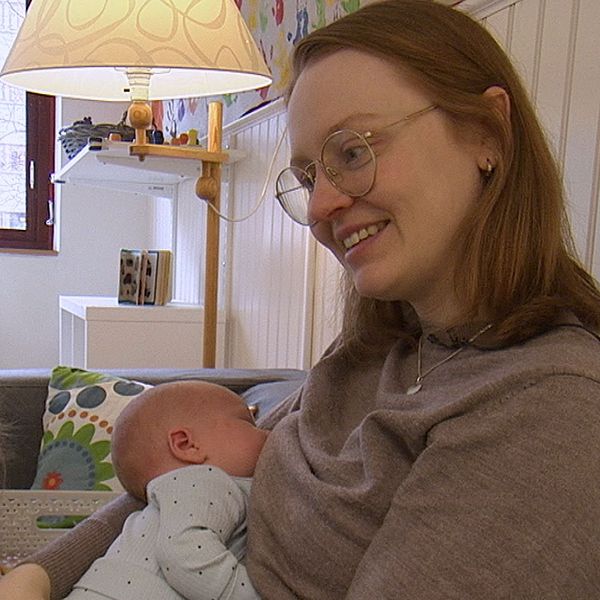 En kvinna håller en baby i famnen, ett barn sitter bredvid.