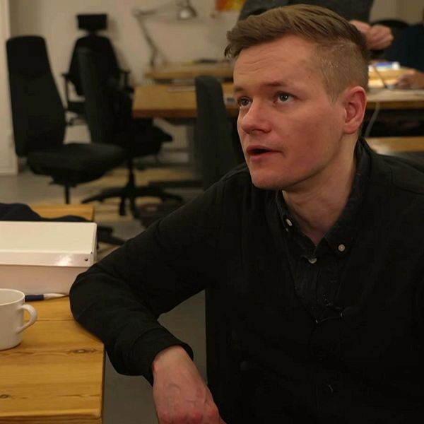 Joakim Medin sitter vid ett bord på ett kontor och reagerar på uppskjuten rättegång.