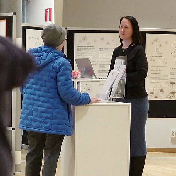 En person går förbi kameran medan en annan ställer frågor till Kristina Kleemo som står vid Luleå kommuns monter på Kulturens hus.