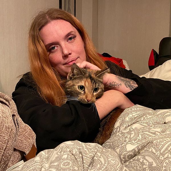 En delad bild som visar två sektioner. Den vänstra sektionen visar en hand som tänder en liten ljuslykta på ett bord, bredvid en grön växt i en kruka. Den högra sektionen visar en person som håller en katt i famnen, insvept i en mjuk filt. Rummet har en varm och mysig atmosfär.