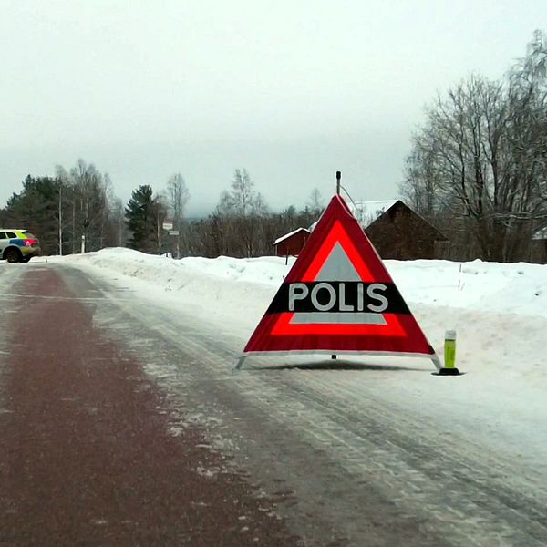 En väg med en uppställd triangel som det står ”polis” på . i bakgrunden syns en polisbil