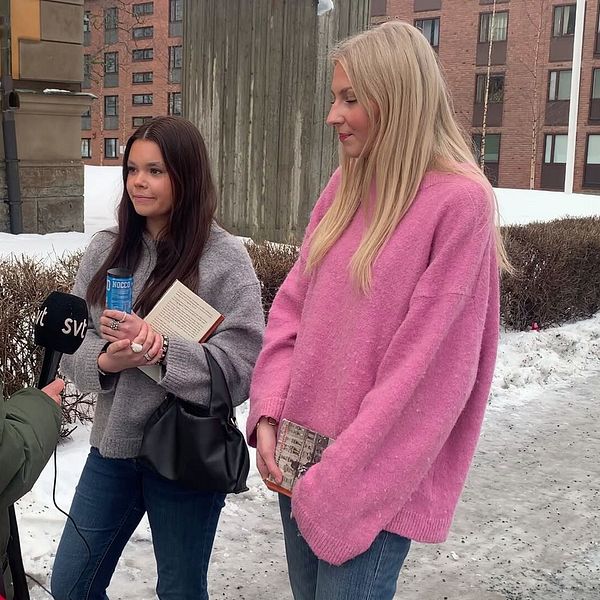 En reporter från SVT intervjuar två personer utomhus på en snöig trottoar. Personen som håller mikrofonen är klädd i en grön jacka och de två intervjupersonerna har på sig vinterkläder, inklusive en grå och en rosa tröja. I bakgrunden syns byggnader.