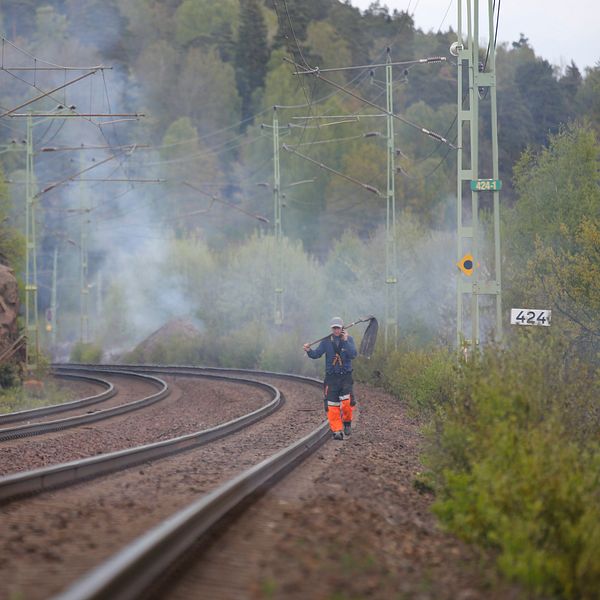 En brandman går på ett järnvägsspår, i bakgrunden ser man brandrök