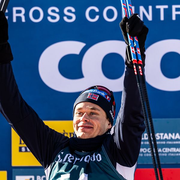 En skidåkare lyfter sina skidor i segergest mot en bakgrund med FIS Cross Country och Coop-loggor.