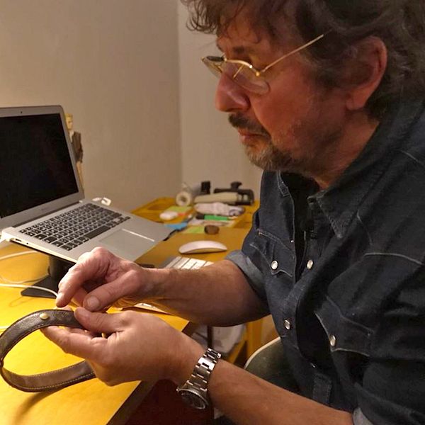 Nära bild på ett hundhalsband med datummärkning. Dennis Dahlqvist sitter vid ett bord och pekar mot halsbandet.
