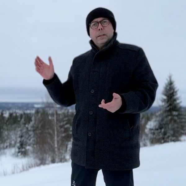 En reporter står med handen och visar i ett vinterlandskap