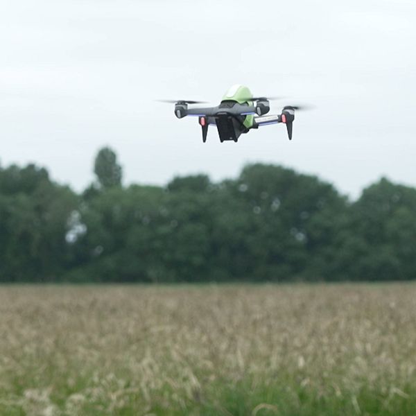 Drönare flyger över ett fält bredvid en kamera eller sensor på stativ.