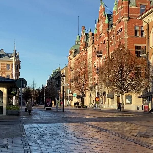 En delad bild som visar två bilder på Sundsvalls stenstad. Till vänster syns en svartvit historisk bild med många människor som promenerar, klädda i tidstypiska kläder från tidigt 1900-tal. Till höger visas en nutida bild av samma gata, där solens strålar belyser moderna byggnader och en lugn atmosfär på en halvmånskad gata med få personer.