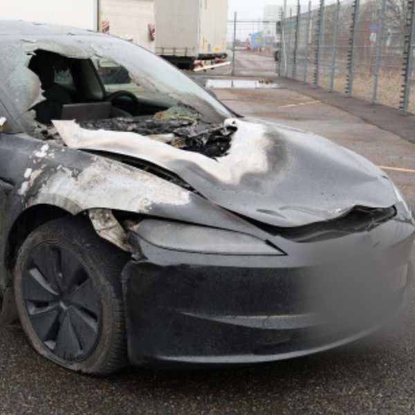 Kraftigt krockskadad svart personbil med bucklig motorhuv och krossat främre fönster.