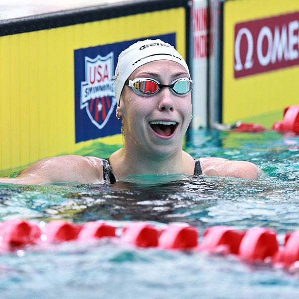 Simmare tar i kanten vid mål efter lopp i simbassäng, USA Swimming-skylt syns i bakgrunden.